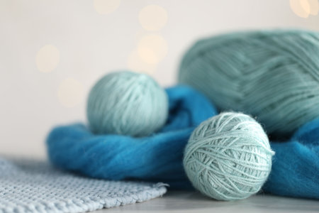 Soft felting wool and knitting yarn on white wooden table against blurred lights, closeupの写真素材