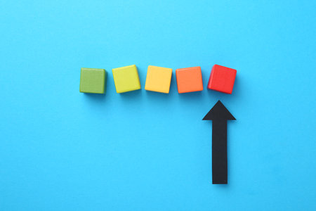 Maximum. Colorful cubes and arrow pointing at red one on light blue background, flat layの写真素材