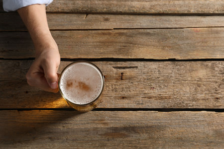 Man with glass mug of beer at wooden table, top view. Space for textの写真素材
