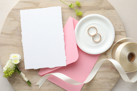 Wedding invitation card, envelope, golden rings, ribbon and floral decor on color textured table, top viewの写真素材