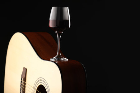 Acoustic guitar and red wine on black background, closeup. Space for textの写真素材