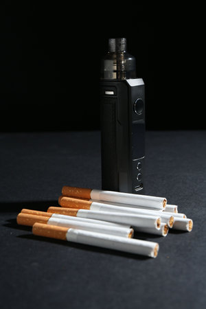 Electronic smoking device and cigarettes on dark table against black background, closeupの写真素材