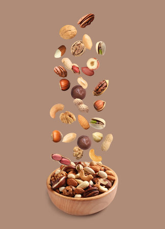 Peanut and other nuts falling into bowl on color backgroundの写真素材