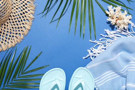 Frame of beach accessories and palm leaves on blue background, flat lay. Space for textの写真素材