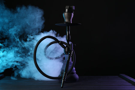 Hookah on wooden table with smoke in color lights against black backgroundの写真素材