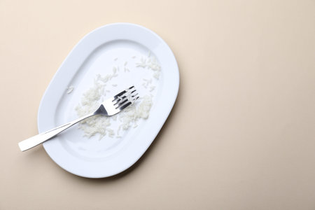 Dirty plate with rice and fork on beige background, top view. Space for textの写真素材