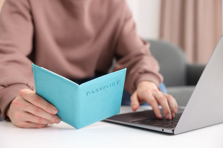 Man with passport using laptop at table indoors, closeupの写真素材