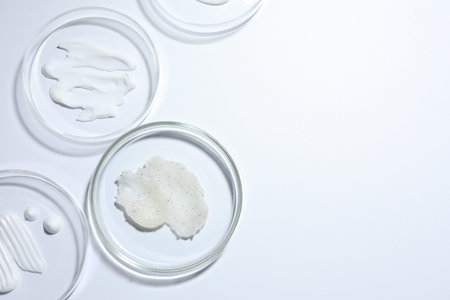 Different cosmetic products in Petri dishes on white background, flat lay. Space for textの写真素材
