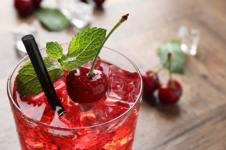Tasty cherry soda with ice cubes, berries and mint in glass on wooden table, closeup. Space for textの写真素材