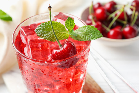 Tasty cherry soda with ice cubes, berries and mint in glass on white wooden table, closeupの写真素材