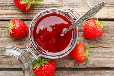 Tasty strawberry jam in glass jar and fresh berries on wooden table, flat layの写真素材