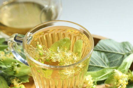 Tasty linden tea in cup, leaves and flowers on light table, closeupの写真素材