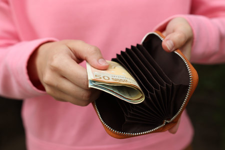 Woman putting money into wallet outdoors, closeup