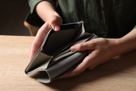 Woman with empty wallet at wooden table, closeup