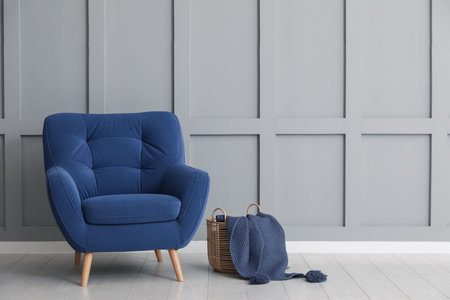 Comfortable blue armchair and basket with cloth near light gray wall indoors, space for textの写真素材