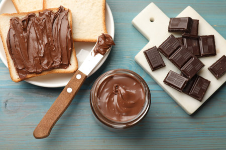 Tasty chocolate butter, pieces, knife and slices of bread on light blue wooden table, flat layの写真素材