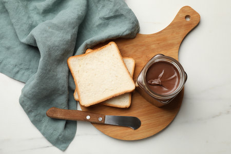 Tasty chocolate butter in glass jar, slices of bread and knife on white marble table, top viewの写真素材