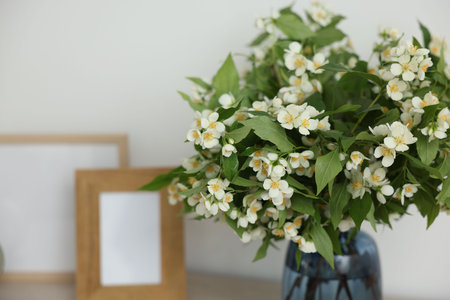 Beautiful jasmine flowers in vase and photo frames on table indoors, closeup. Space for textの写真素材