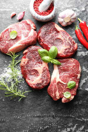 Pieces of raw beef meat and spices on dark table, flat layの写真素材
