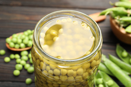 Pickled peas in jar and pods on black wooden table, closeupの写真素材