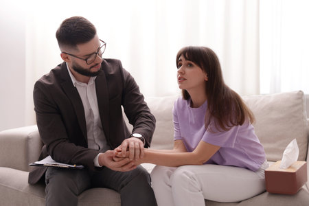 Psychologist supporting patient during therapy session on sofa in office