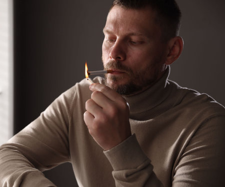 Man lighting cigarette with match near window indoorsの写真素材