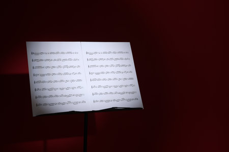 Note stand with music sheets on dark red background, space for textの写真素材