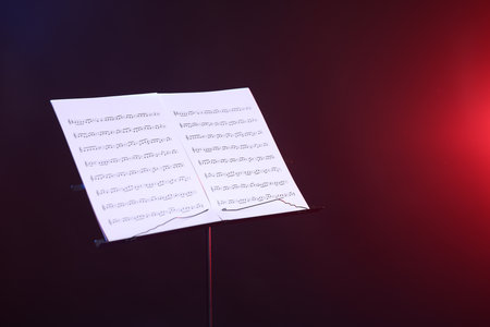 Stand with music sheets in neon lights on dark background, space for textの写真素材