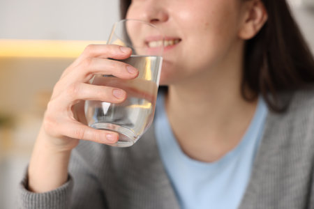 Woman drinking water from glass in kitchen, closeupの写真素材
