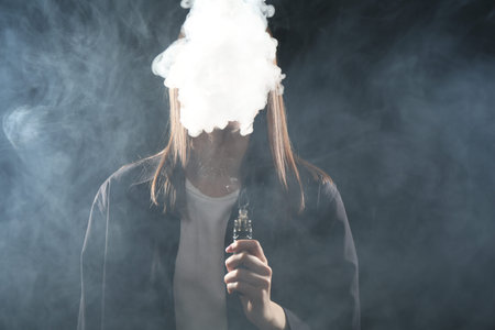 Woman using electronic smoking device on dark background