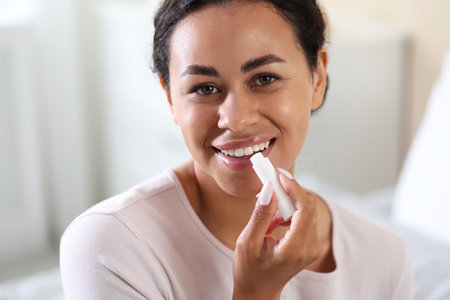 Smiling woman applying lip balm onto her lips on blurred background, closeupの写真素材