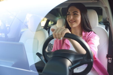 Woman behind steering wheel of modern car, view through windshield