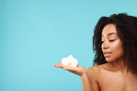 Portrait of beautiful Brazilian woman with orchid flower after spa treatment on light blue background. Space for textの写真素材