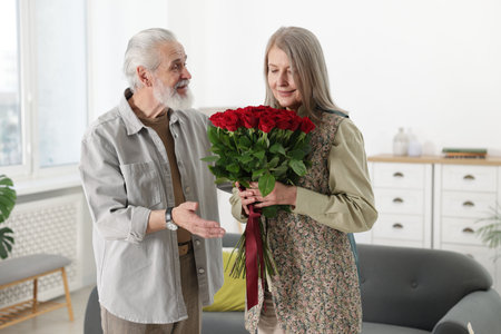 Happy couple with bouquet of red roses at homeの写真素材