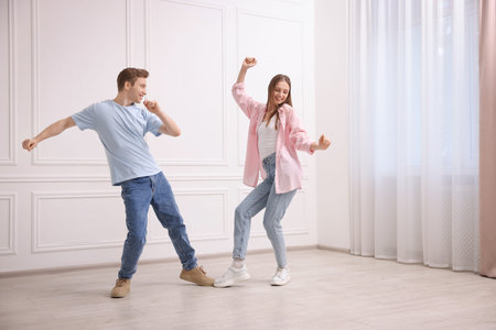 Happy couple dancing together near white wall at homeの写真素材