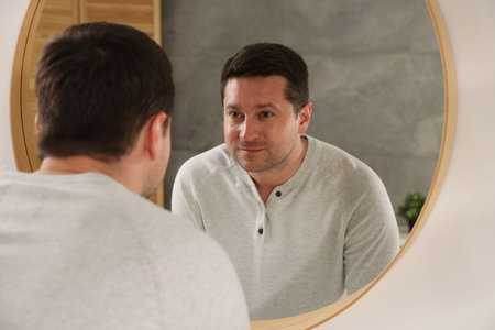 Handsome man looking at himself in mirror indoors