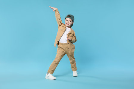 Happy little boy in baseball hat dancing on light blue backgroundの写真素材