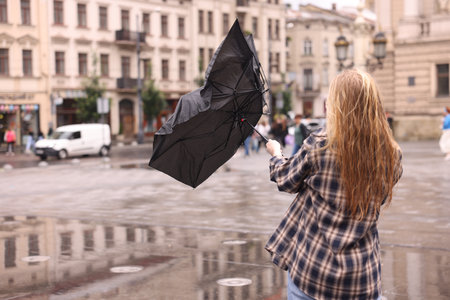 Woman with broken umbrella on city street, back view. Space for textの写真素材