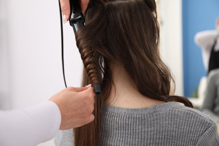 Hairdresser curling woman's hair in salon, closeupの写真素材