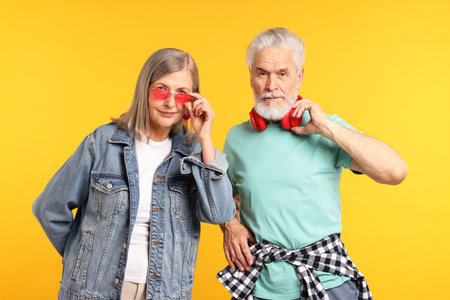 Senior couple in stylish outfits on orange background