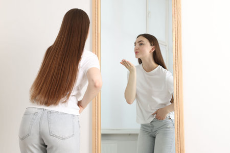 Beautiful woman blowing kiss near mirror indoorsの写真素材