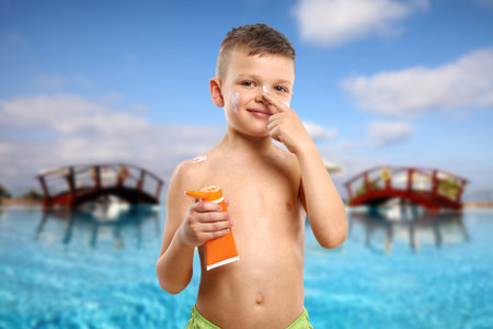 Little boy applying sun protection product on his face by outdoor swimming poolの写真素材