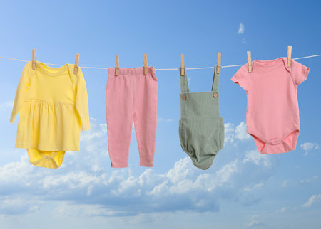 Different baby clothes drying on washing line against blue skyの写真素材
