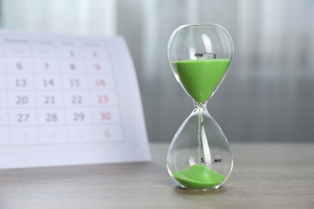 Deadline. Hourglass with flowing sand and calendar on wooden table indoorsの写真素材