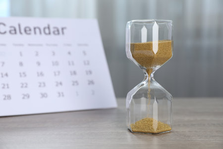 Deadline. Hourglass with flowing sand and calendar on wooden table indoorsの写真素材