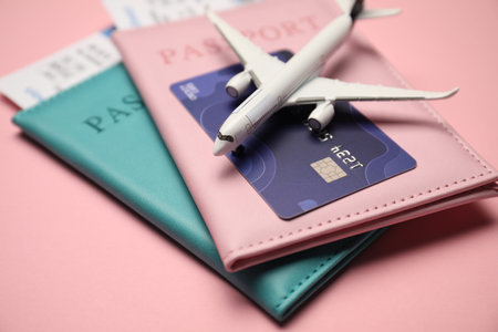 Passports with tickets, credit card and airplane model on pink background, closeup