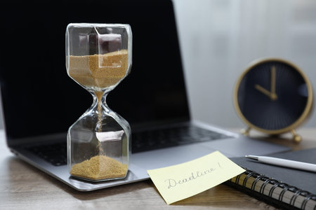 Sticky note with word Deadline, hourglass, alarm clock, stationery and laptop on wooden table...