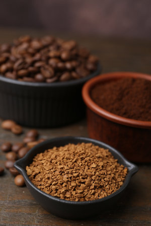 Different types of instant coffee and beans in bowls on wooden table against brown background, closeupの写真素材