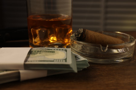 Mafia and criminal world. Money, ashtray with cigar and whiskey on wooden table, closeupの写真素材
