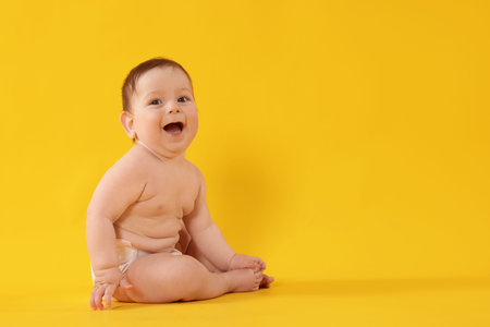 Cute little baby in diaper sitting on yellow background. Space for text